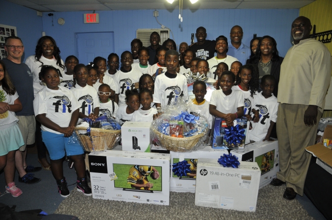 the Orlando Magic and Magic guard Victor Oladipo surprised youth and representatives from the New Image Youth Center (NIYC) in Parramore with all new equipment including big screen TVs, video games and computers after most of these items were stolen earlier in the week. Pictured: Victor Oladipo (center), City Commissioner Regina Hill (right), New Image Youth Center Founder/Executive Director Shanta Barton-Stubbs (far left), Magic Community Ambassadors Nick Anderson (back left) and Bo Outlaw (back right) and NIYC youth. Photo taken by Gary Bassing.